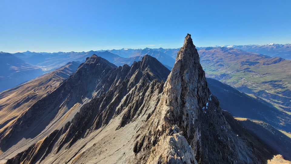 Berggipfel mit scharfem Grat und Fernblick in die Alpen.