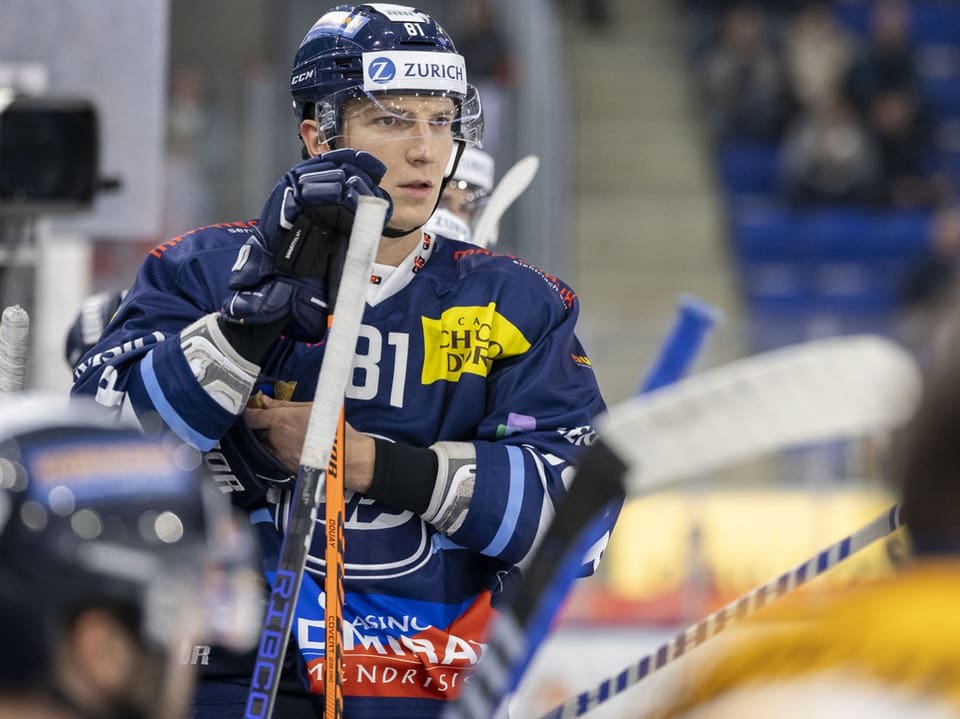 Ein Eishockeyspieler in blauem Trikot hält sich an der Spielerbank fest.