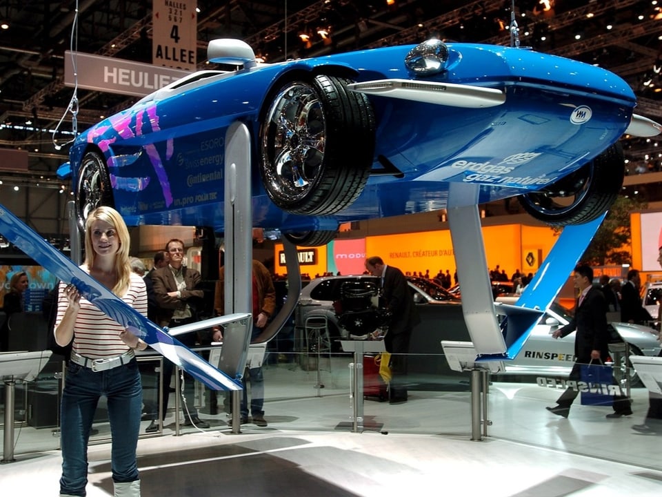 Frau steht vor einem blauen Auto bei einer Ausstellung.