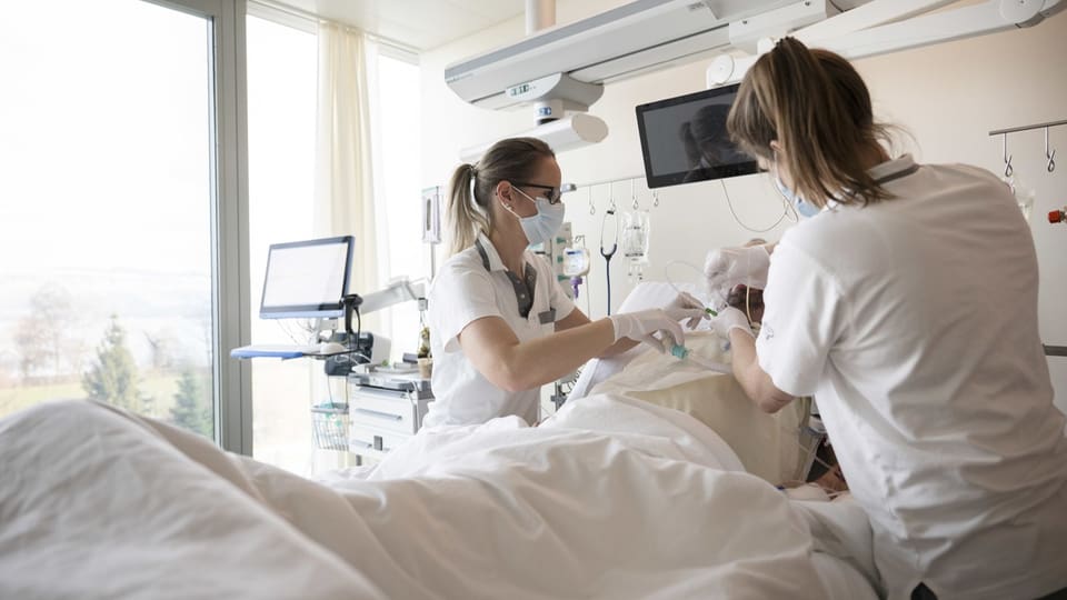 Zwei Krankenschwestern kümmern sich um einen Patienten im Krankenhauszimmer.