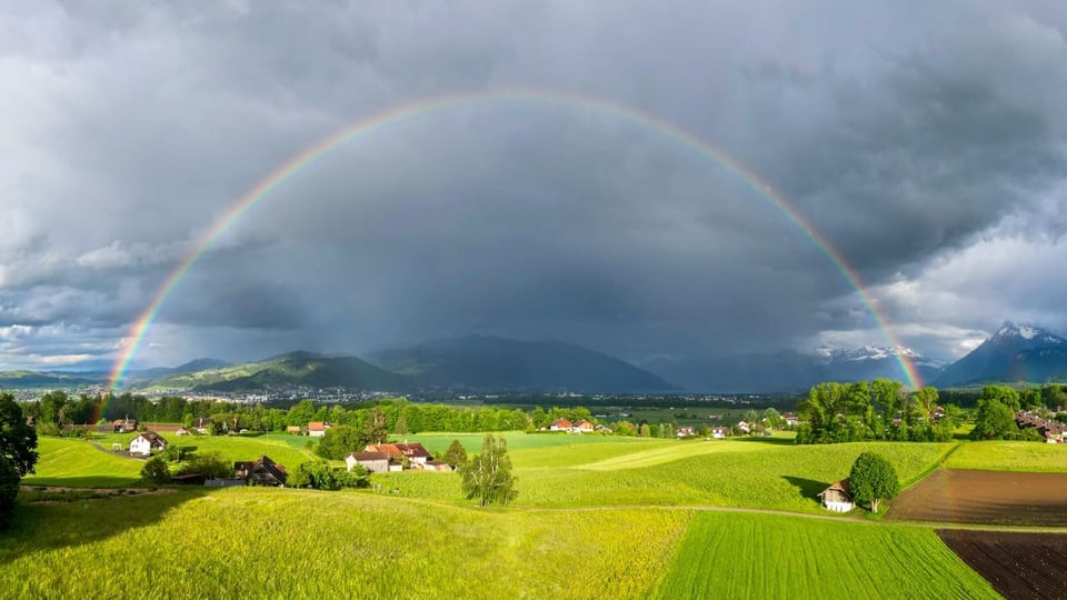 Landschaft mit Regenbogen über Feldern und Bergen.