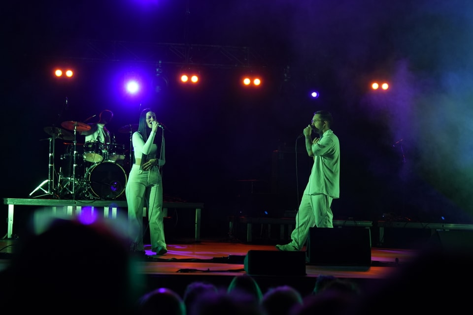 Musiker auf Bühne bei Konzert mit bunten Lichtern.