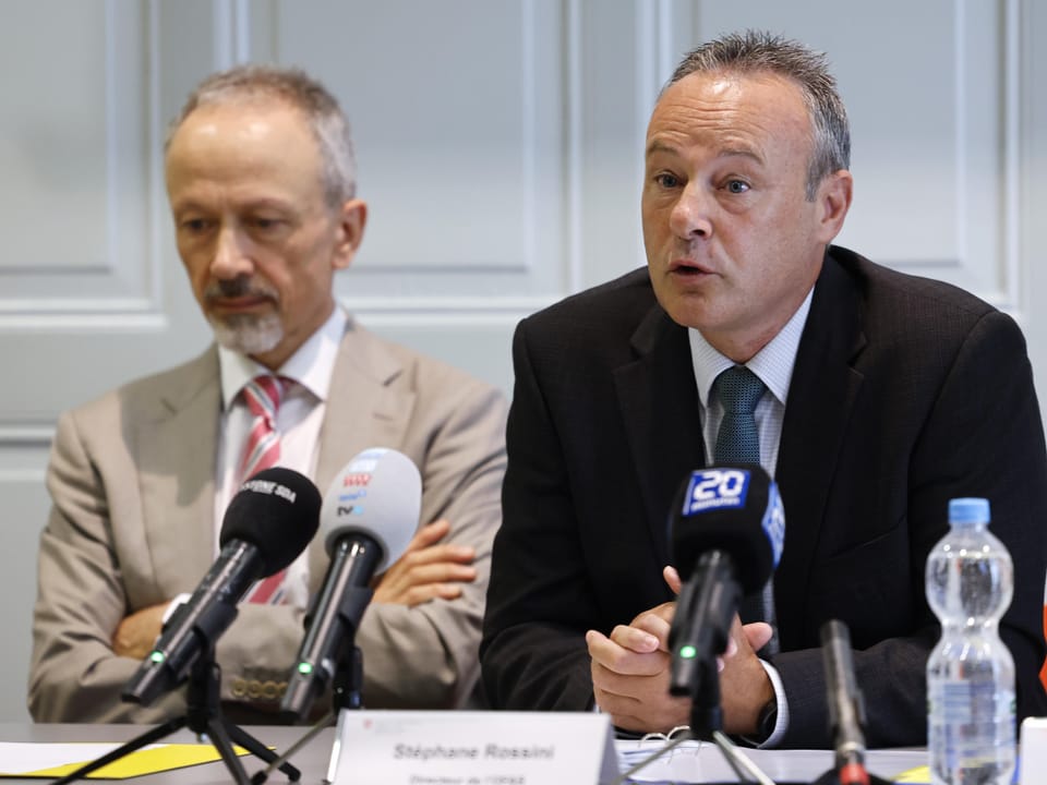 Zwei Männer bei einer Pressekonferenz, beide vor Mikrofonen sitzend.