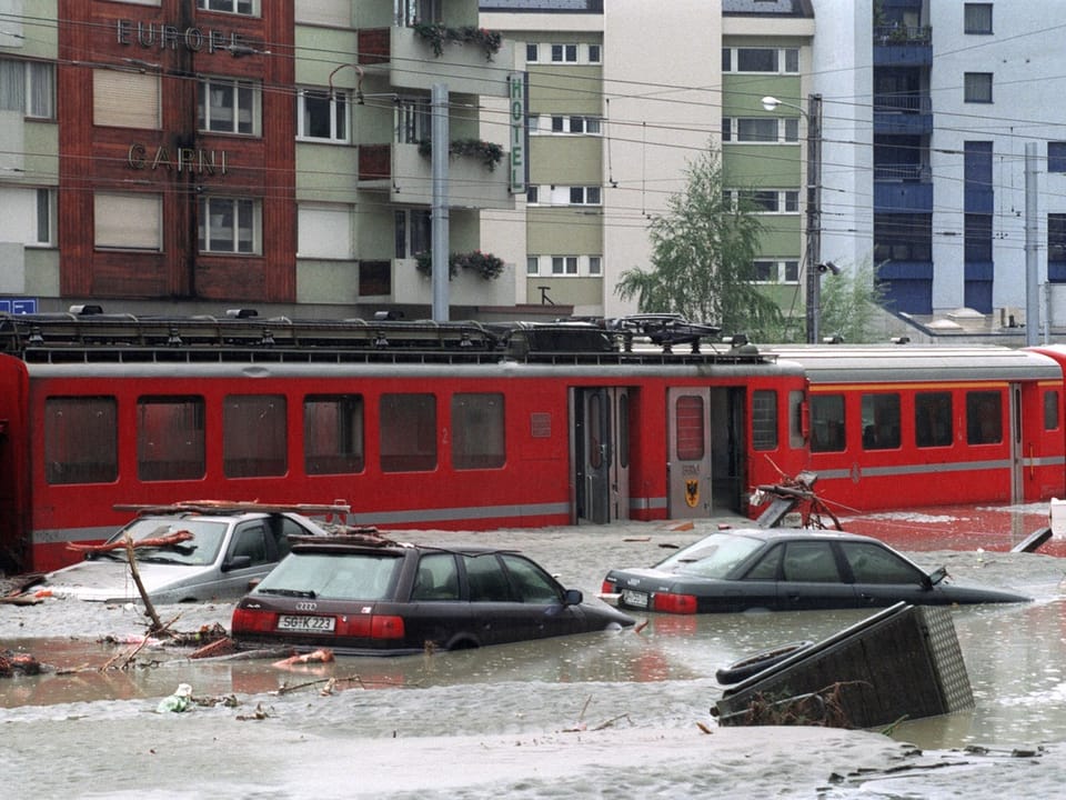 Roter Zug und Autos in überfluteter Stadtstrasse.