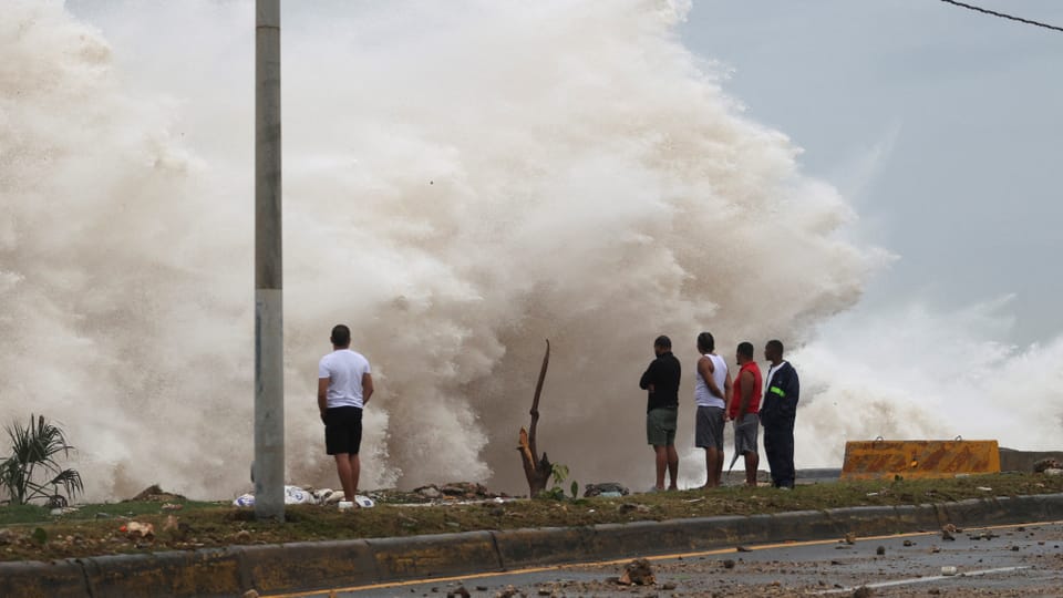 Menschen beobachten riesige Wellen, die auf eine Küste treffen.