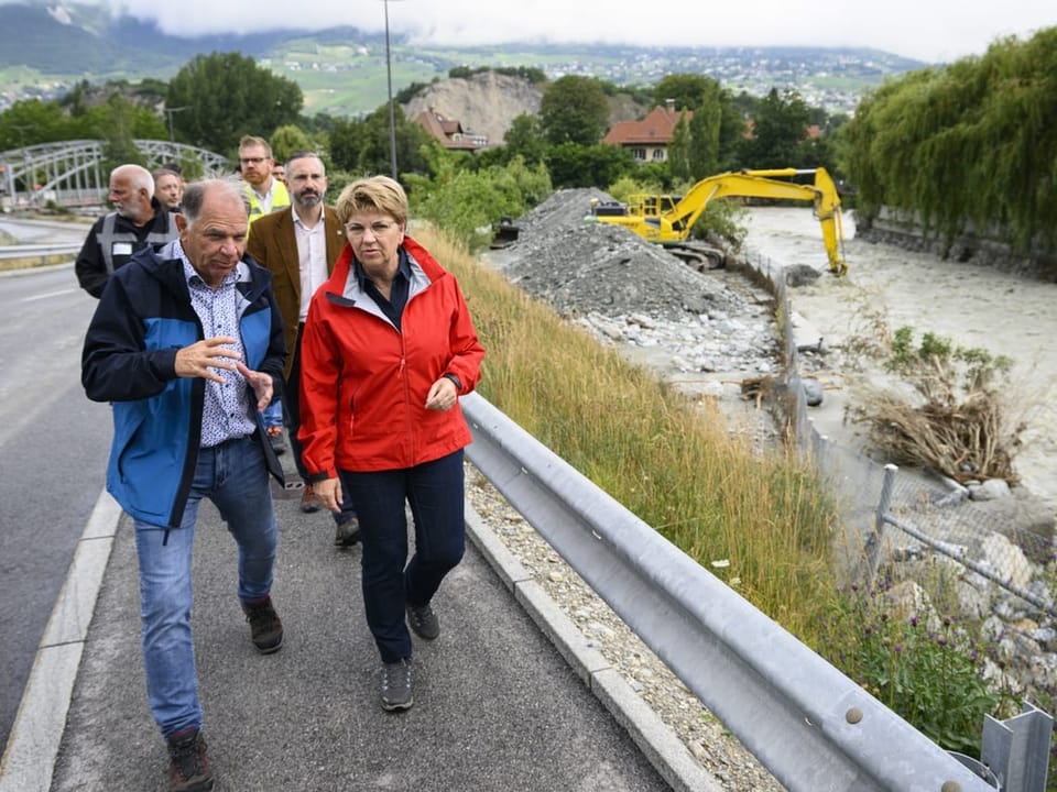 Viola Amherd geht mit Behördenvertretern im Wallis über eine Brücke.