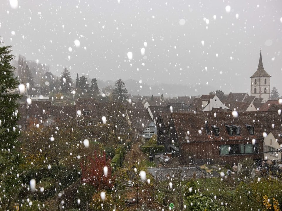 Schneefall über einer Stadt mit Kirchturm im Hintergrund.