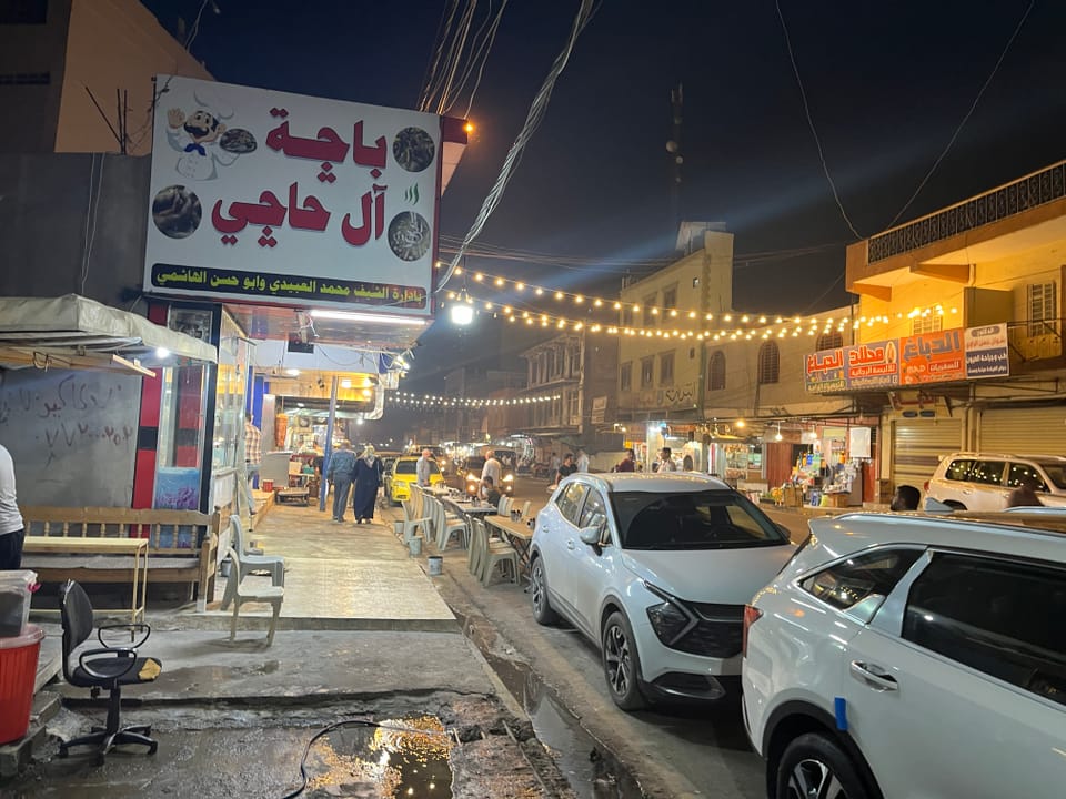 Strassenansicht bei Nacht mit Ladenfronten und geparkten Autos in einer Stadt im Nahen Osten.