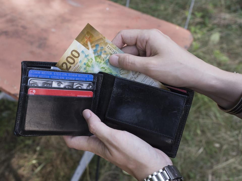 Hände nehmen Schweizer Franken aus einem schwarzen Lederportemonnaie.