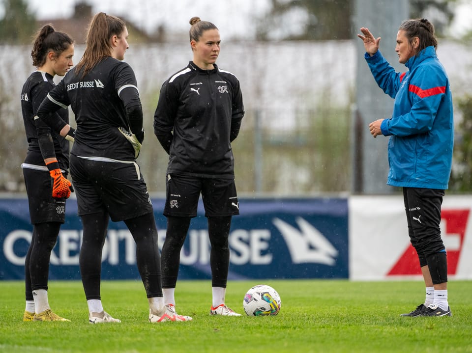 Frauenfussballteam im Gespräch mit Trainerin auf dem Spielfeld.