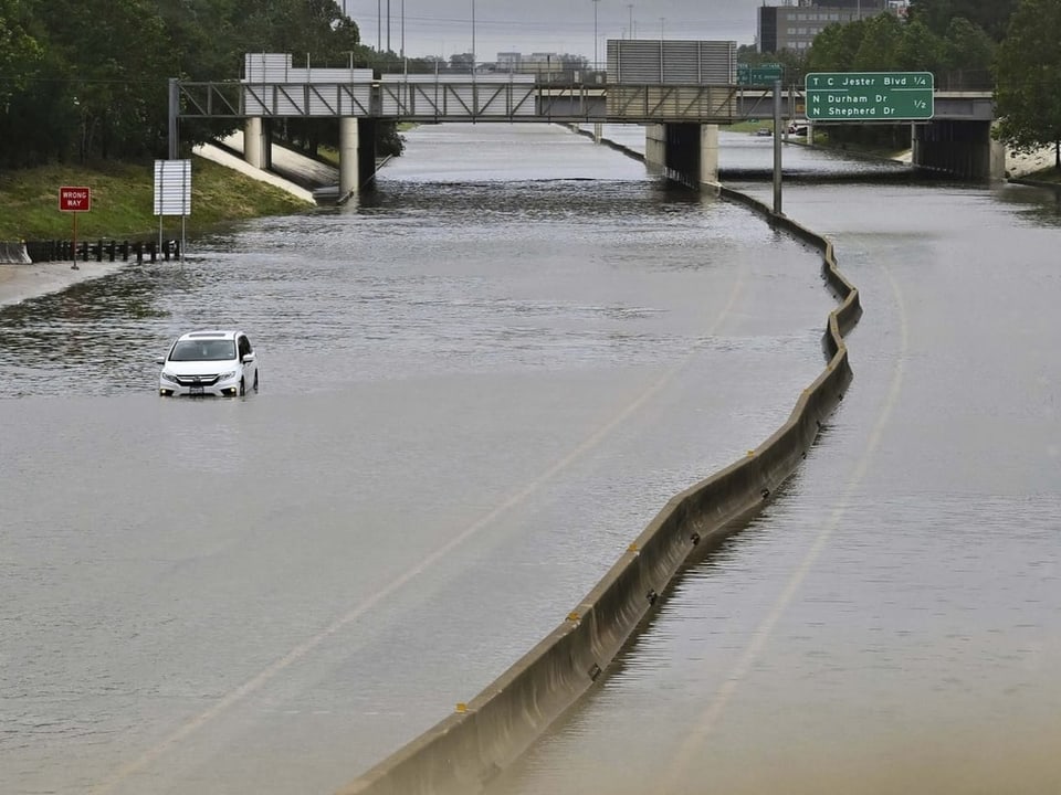 Eine Autobahn überflutet mit Wasser. Nur ein Auto steht auf der Autobahn. 