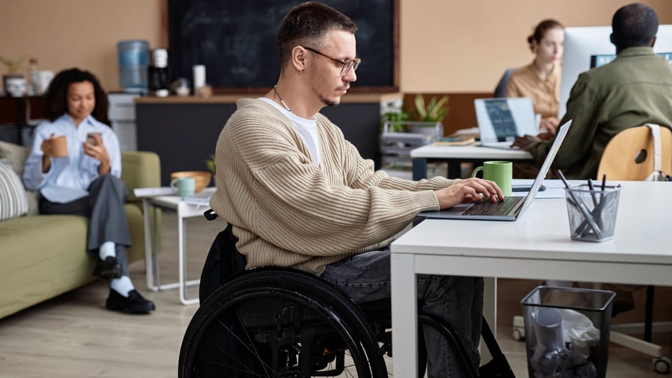 Mann im Rollstuhl arbeitet an Laptop im Büro.