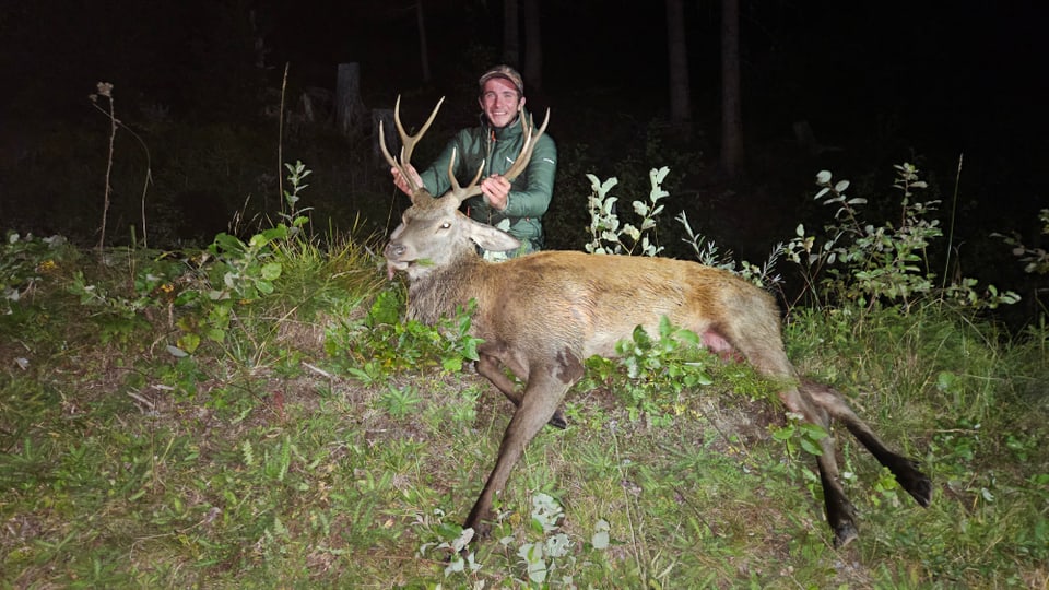 Mann posiert mit erlegtem Hirsch im Wald bei Nacht.