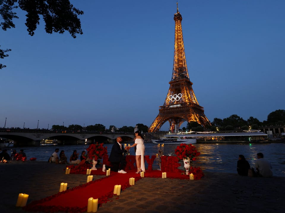 Ein Mann macht einer Frau vor dem Eiffelturm in Paris einen Heiratsantrag.
