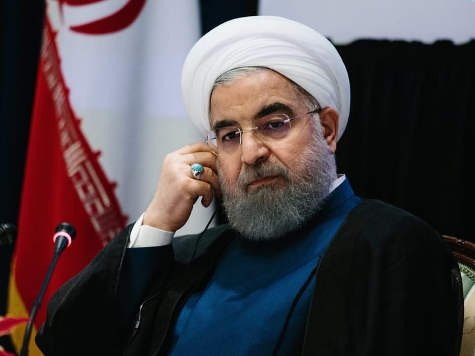 Ruhani sitzt vor Mikrofonen und und stützt seinen Kopf mit seiner mit einem hellblauen Ring bestückten Hand auf.