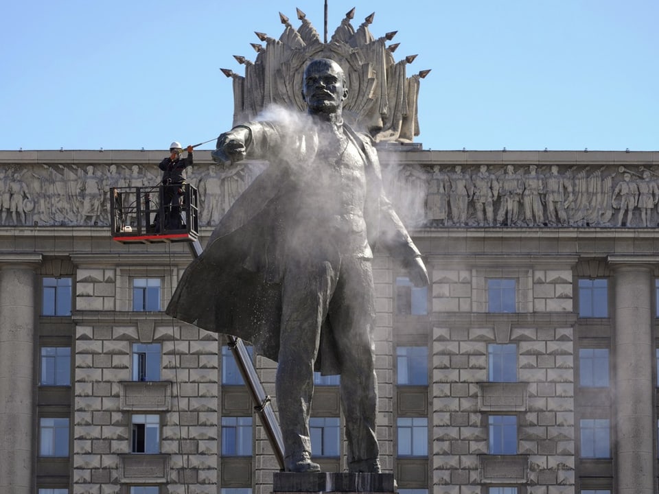 Steinerne Statue von lenin, Kopf mit Seife bedeckt, ein Mann bürstet seinen Mund.