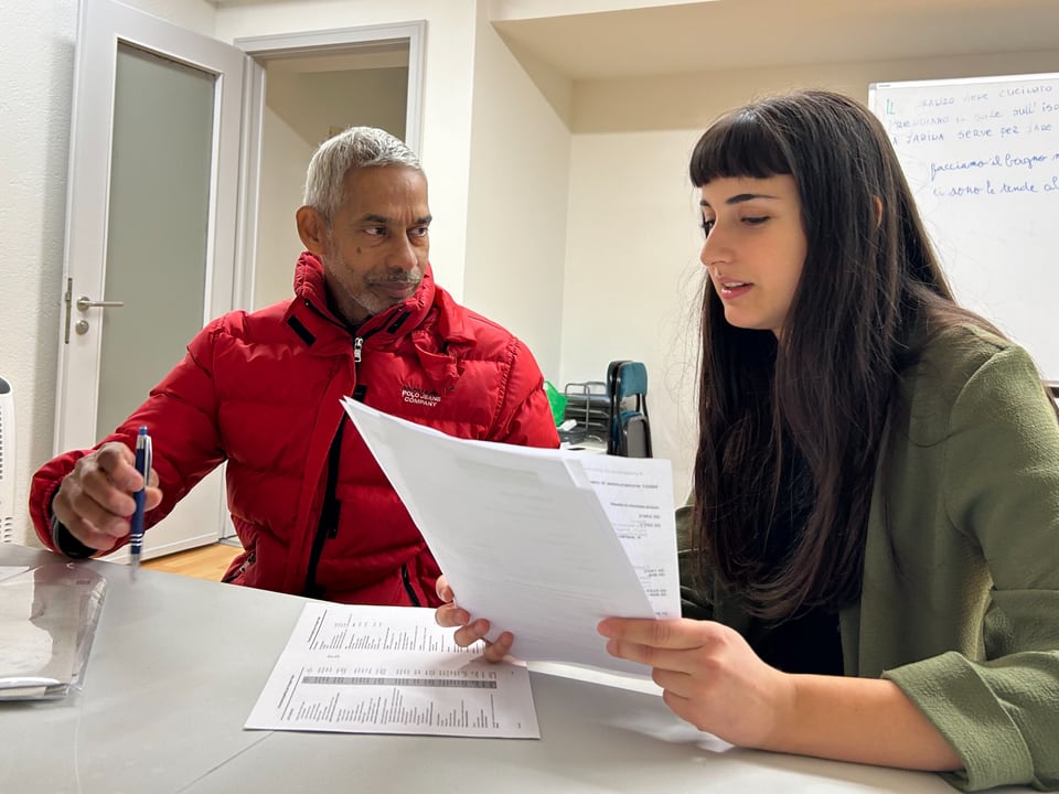 Zwei Personen bei einem Bürogespräch mit Papieren.