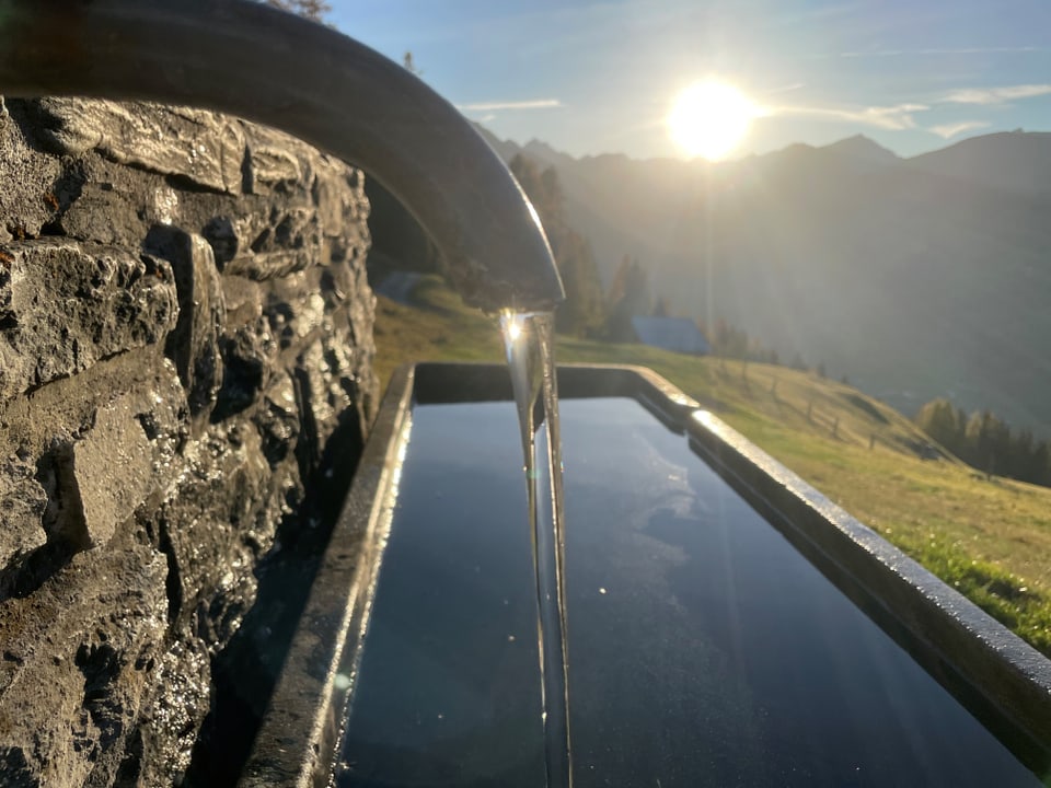 Wasser fliesst aus einem Brunnenrohr in die Berglandschaft bei Sonnenaufgang.