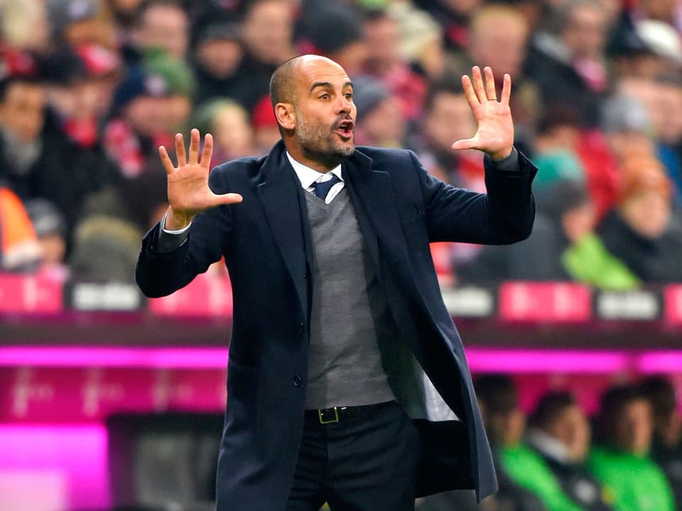 Bayern-Trainer Pep Guardiola gibt seinem Team von der Seitenlinie aus Anweisungen und hält dabei beide Hände in die Luft.