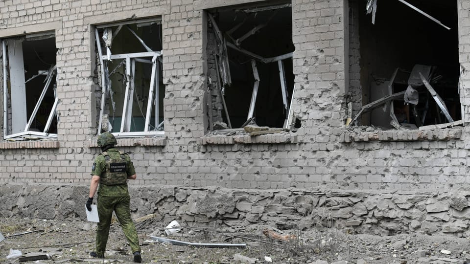 Ukrainischer Soldat vor beschädigtem Gebäude mit zerbrochenen Fenstern.