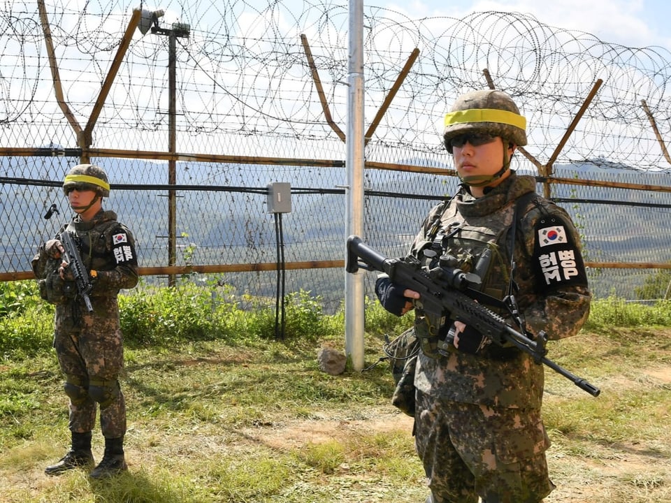 Südkoreanische Soldaten mit Gewehren patrouillieren an einem Stacheldrahtzaun.