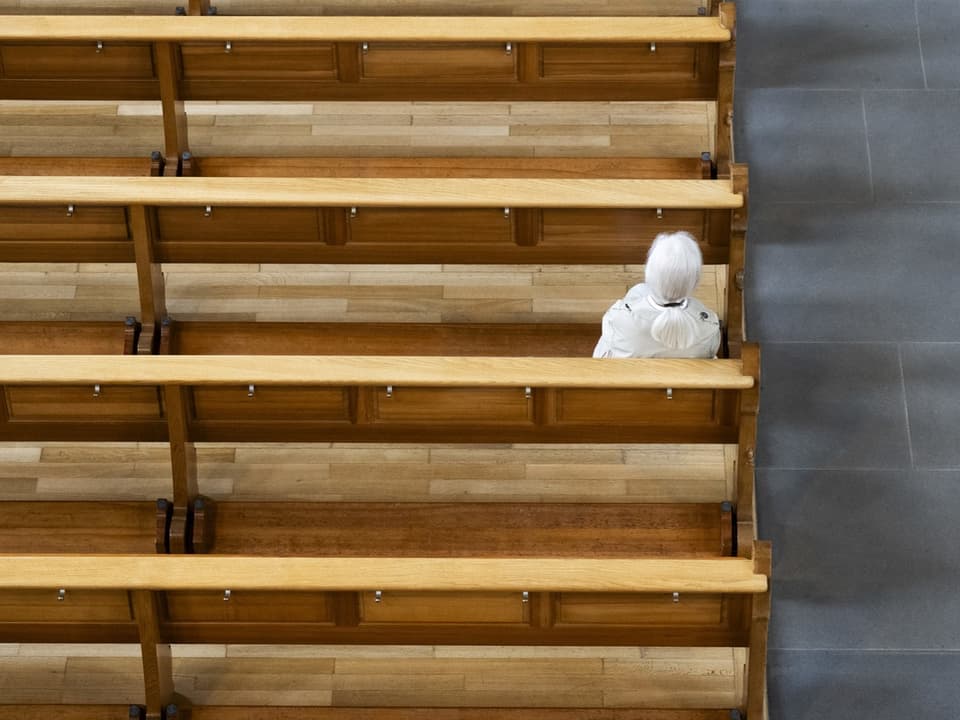 Frau sitzt allein auf Bank in Kirche.