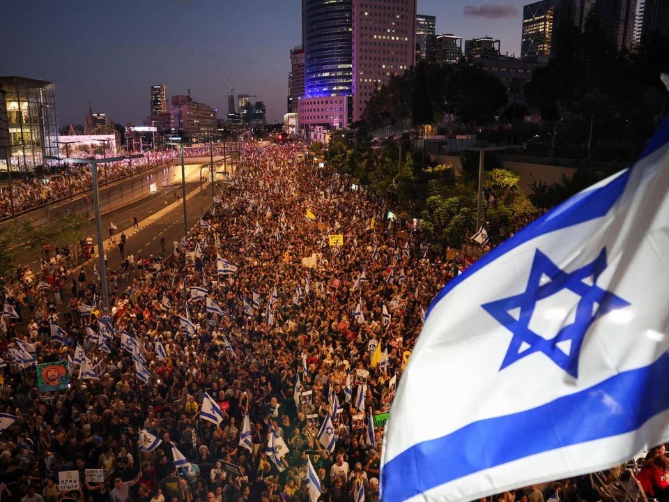 Menschenmenge bei Protest in Tel Aviv mit israelischer Flagge im Vordergrund.