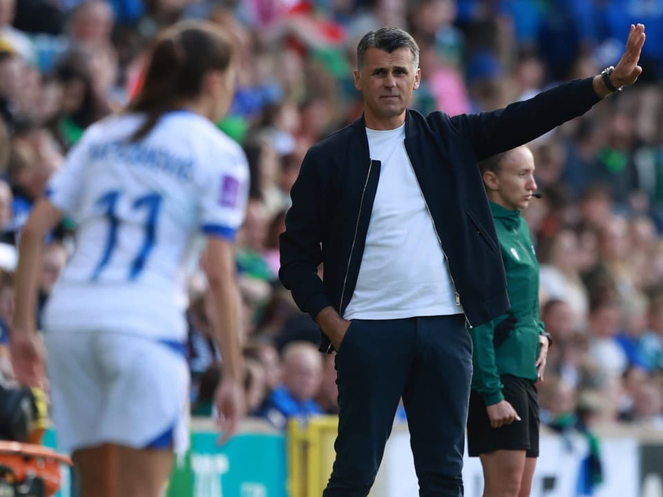 Trainer gibt Anweisungen am Spielfeldrand, Spielerin im Vordergrund.