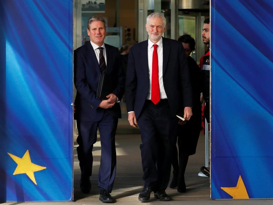 Zwei Männer in Anzügen gehen durch einen Eingang mit EU-Flaggen.