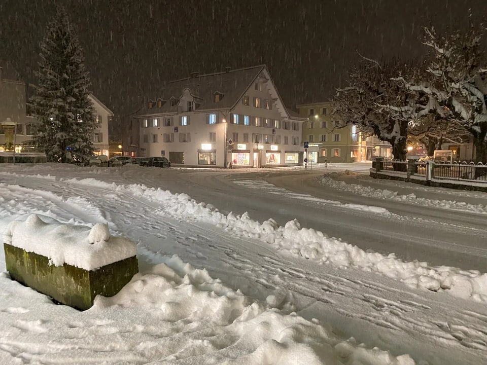 Schneebedeckte Strasse und Gebäude bei Nacht.