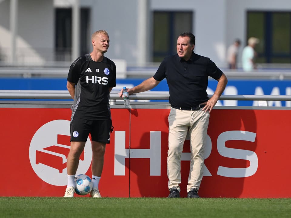 Zwei Männer stehen vor einer HRS-Werbebande auf einem Fussballplatz.