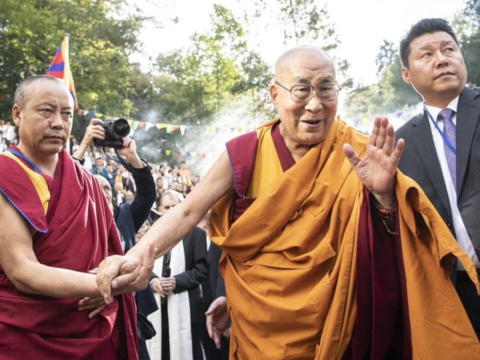 Der Dalai Lama geht mit der Unterstützung eines Mannes