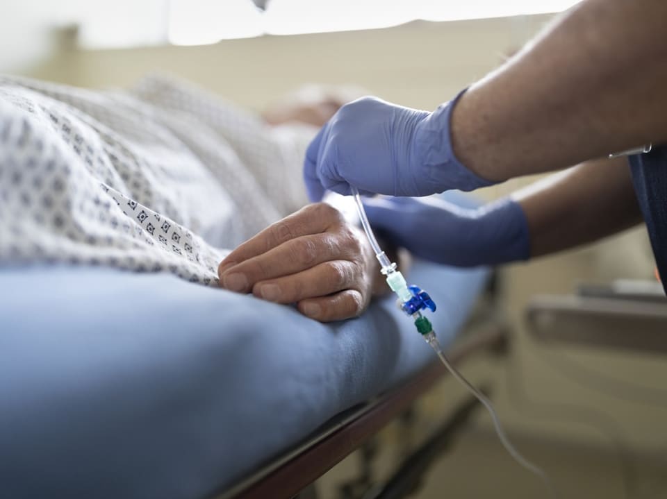 Hand einer Person mit intravenösen Zugang, die auf einem Krankenhausbett liegt.