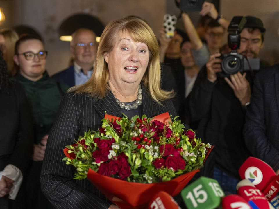 Frau mit Blumenstrauss vor Journalisten und Kameras.