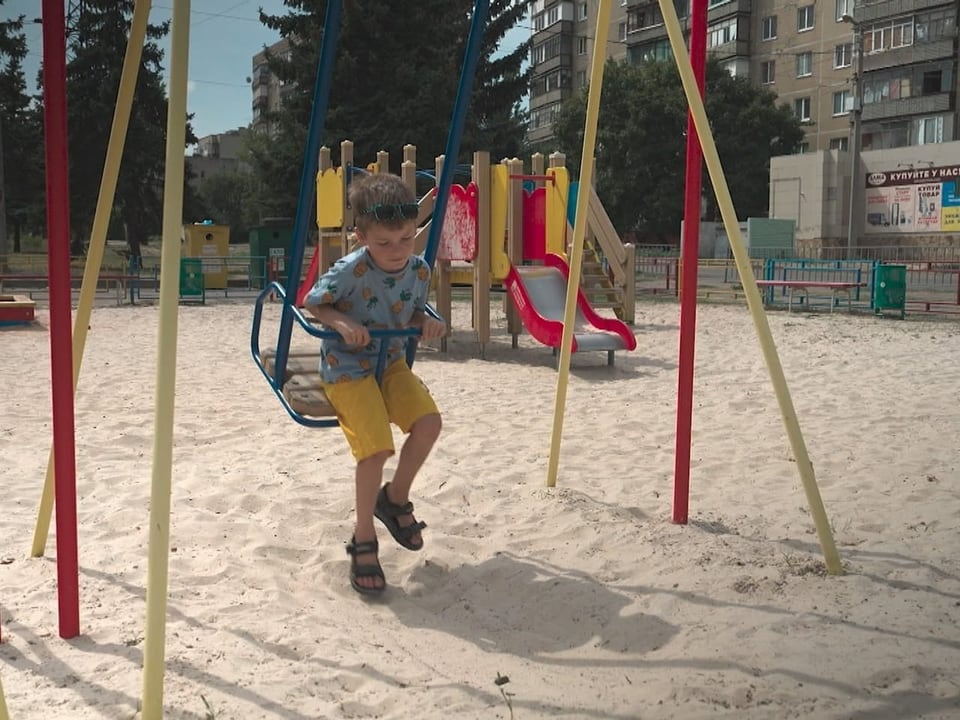 Kind schaukelt auf einem Spielplatz im Sand.