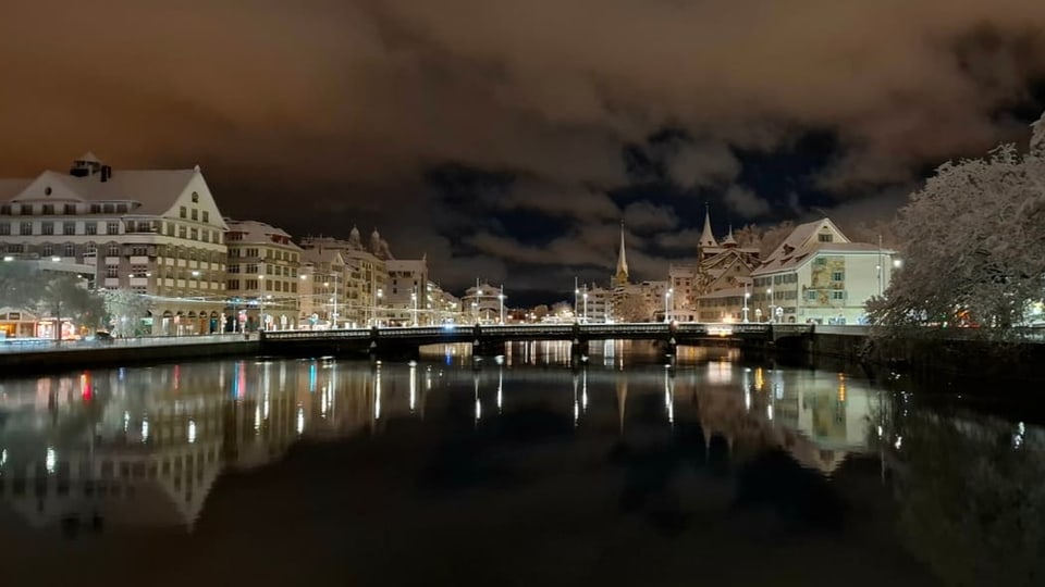 Abendliche Stadtansicht mit Wasserreflexionen und beleuchteten Gebäuden.