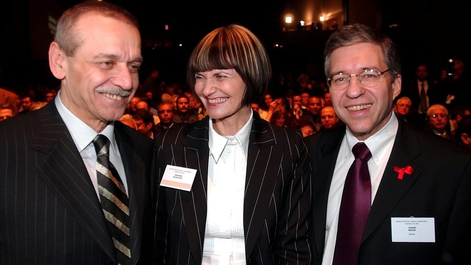 Drei Personen in formeller Kleidung auf einer Veranstaltung lächeln.