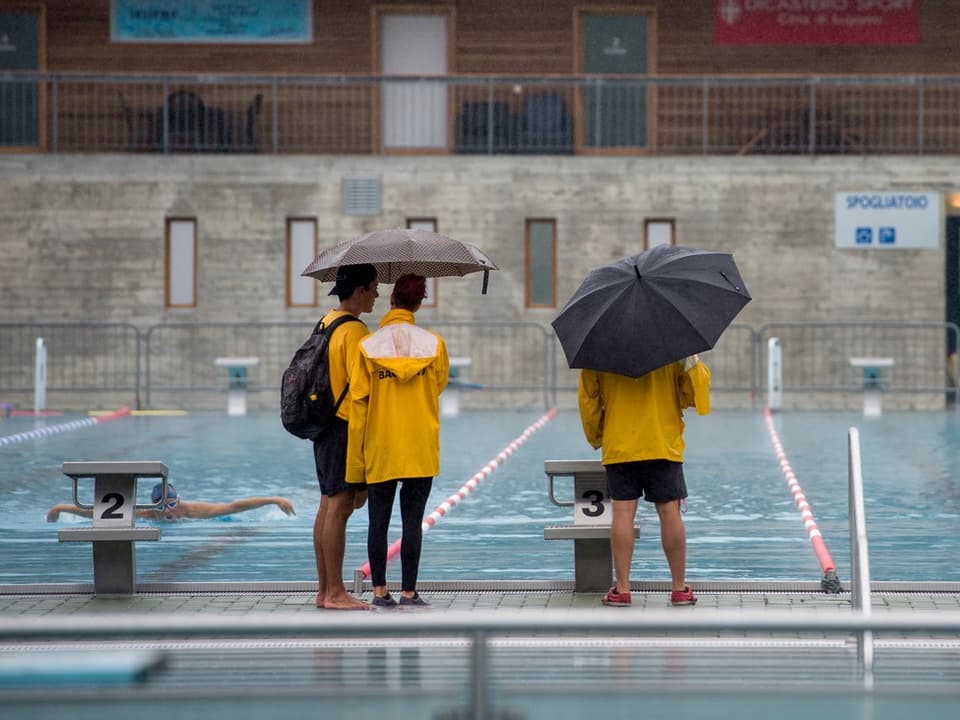 Personen mit Regenschirm vor Schwimmbecken.