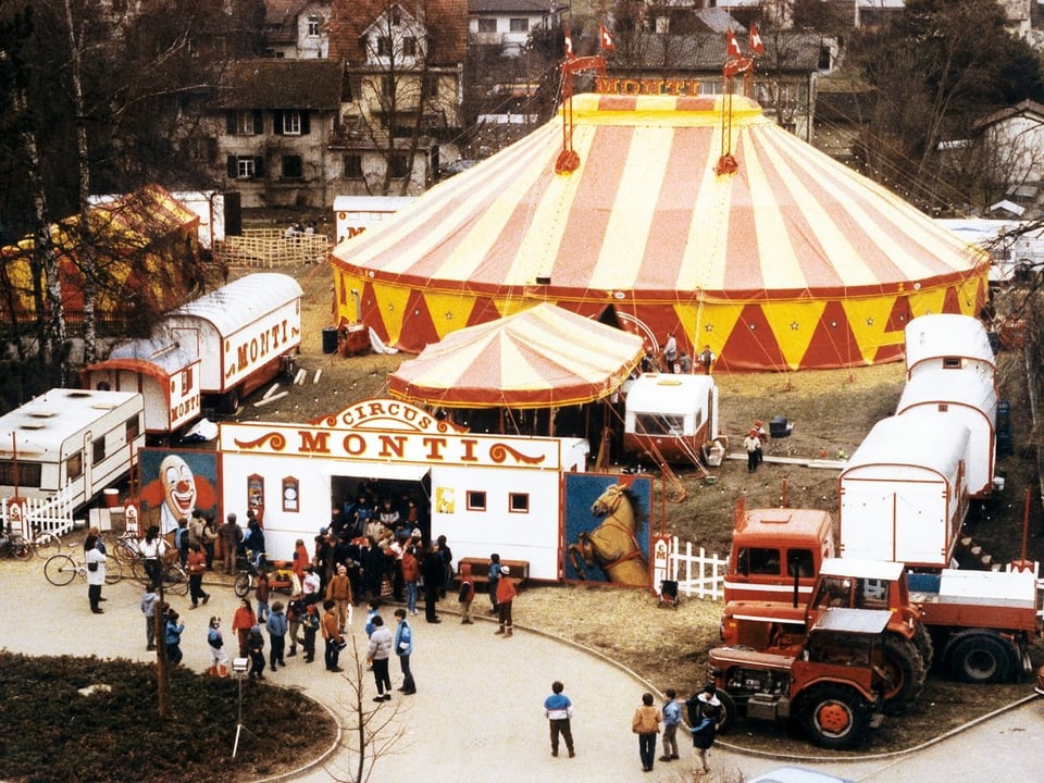 Ein älteres Foto von einem Zirkuszelt und Zirkuswagen rundherum. 