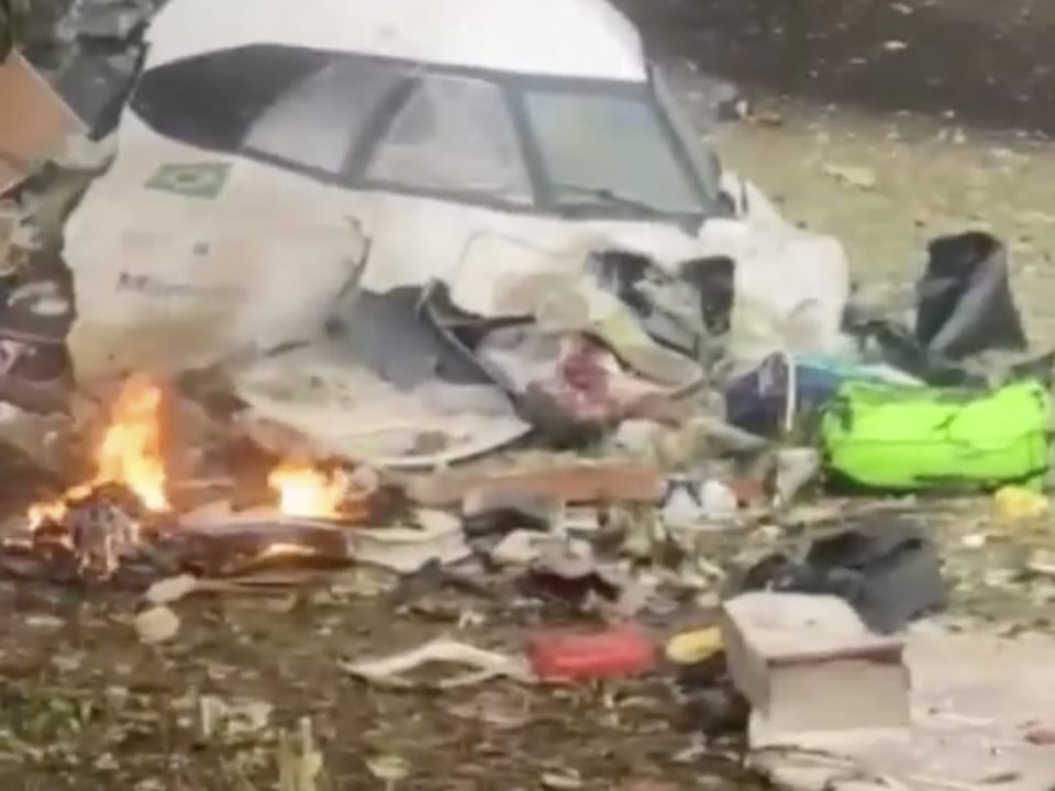 Zerstörter Rennwagen mit Trümmerteilen und Feuer.