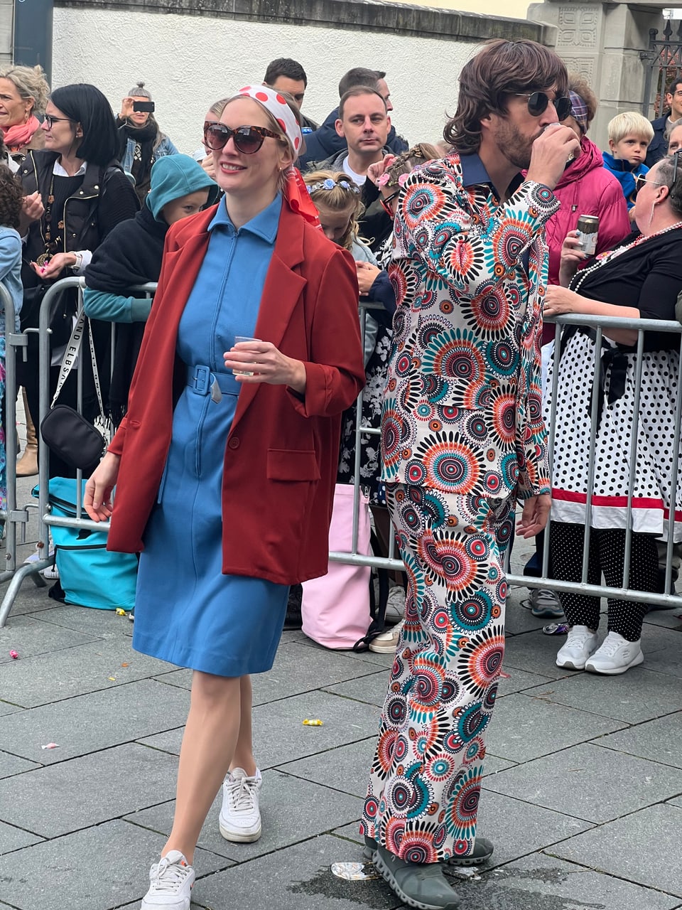 Zwei Menschen in farbigen Outfits gehen auf einer Veranstaltung.