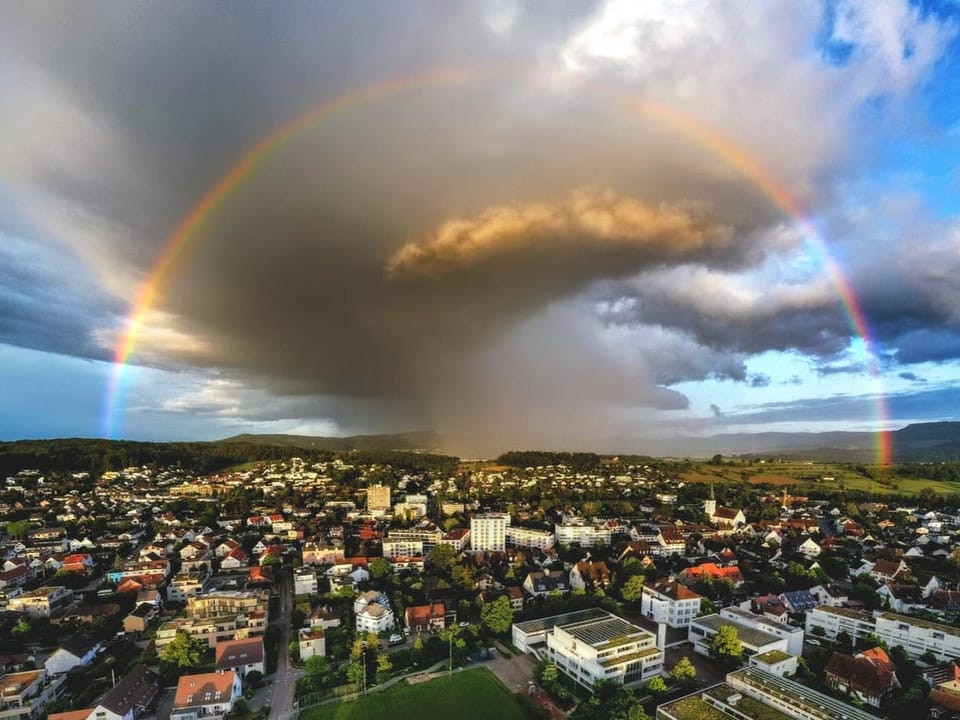 Luftaufnahme einer Stadt unter einem Regenbogen mit dunklen Wolken.