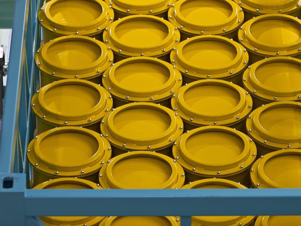 Gelbe Fässer stehen aneinandergereiht in einem Korb aus Metall.