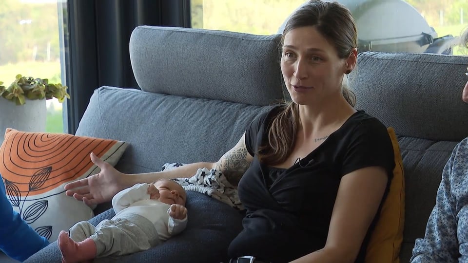 Sophie und ihr Baby auf einem grauen Sofa, im Hintergrund Fenster.