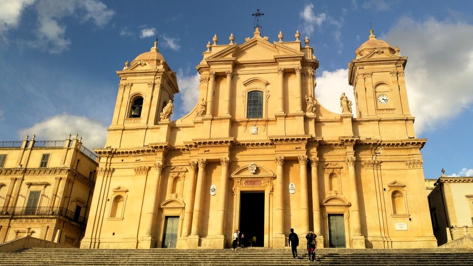 Eine grosse gelbliche Kathedrale mit Statuen, Säulen und Türmen. 