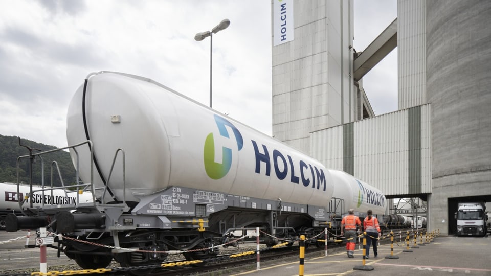 Zwei Mitarbeiter laufen einem Güterwaggon des Zementherstellers Holcim entlang.