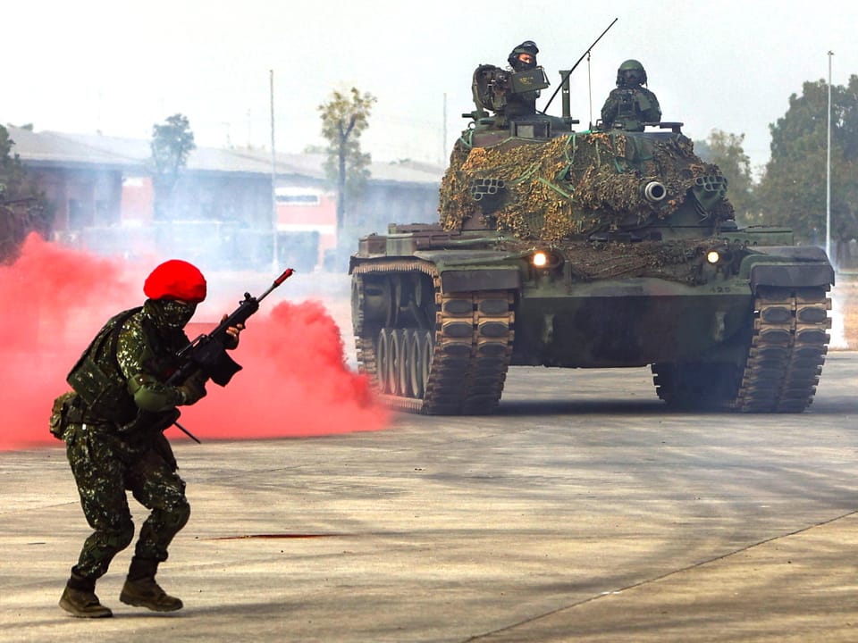 Militärübung: Ein Soldat mit Waffe neben einem Panzerfahrzeug, daneben roter Rauch.