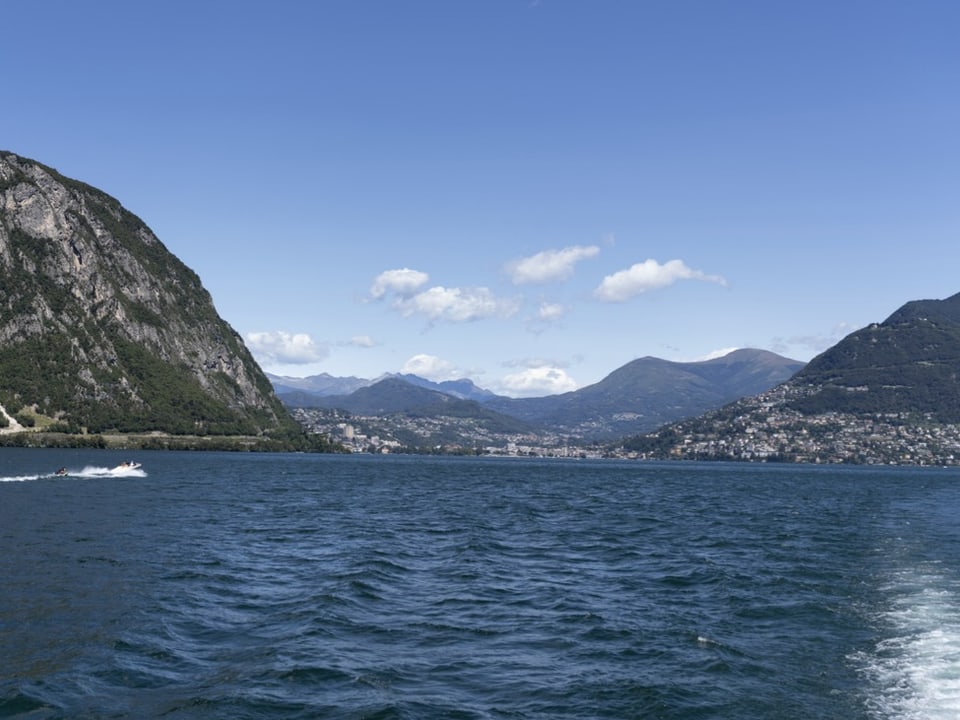 Die Stadt Lugano und die Berge um den Luganersee von einem Schiff aus fotografiert.