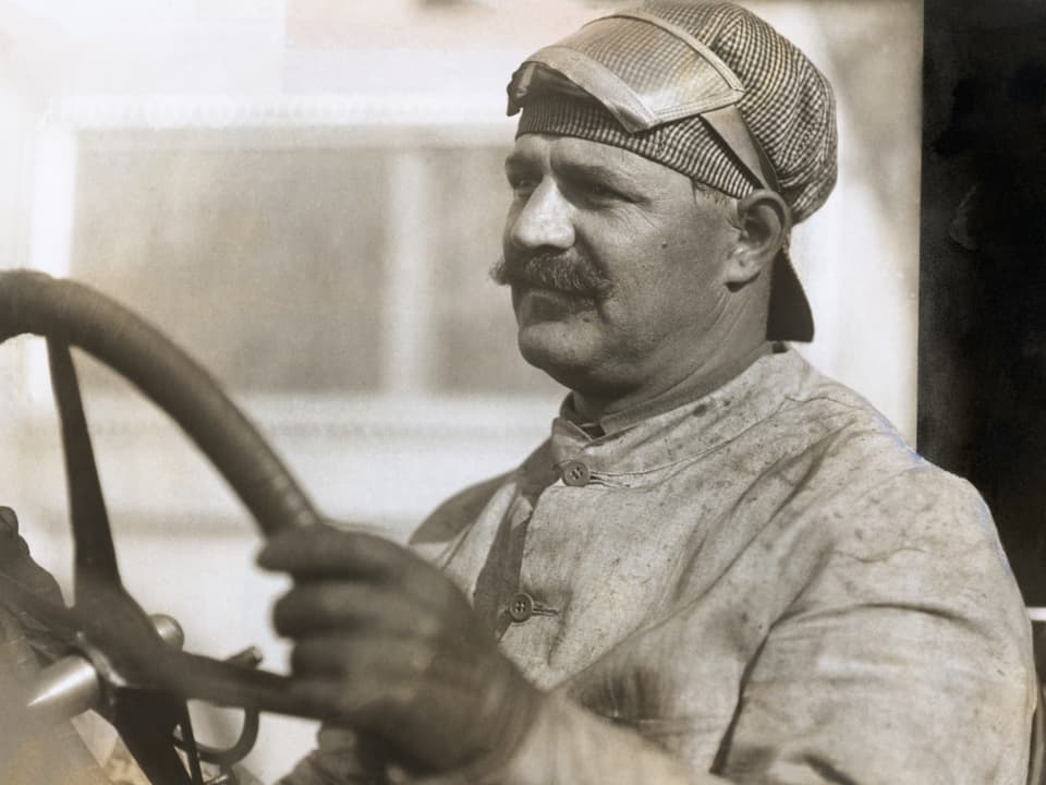 Louis Chevrolet hält das Lenkrad eines Autos.