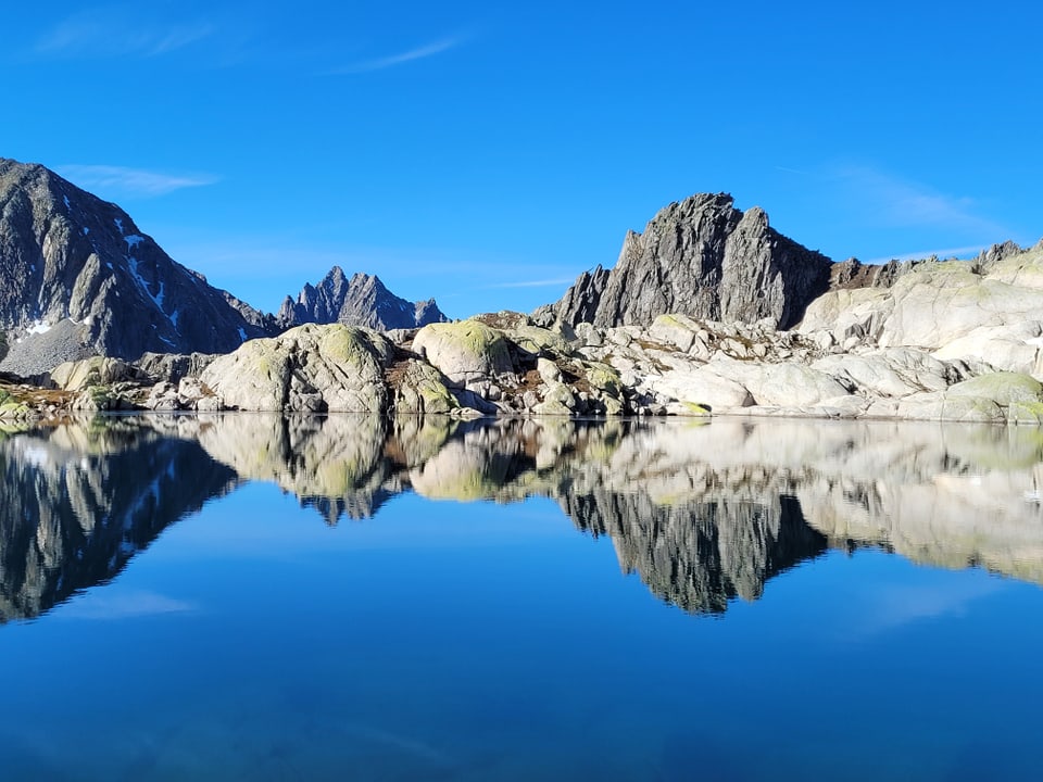 Berge spiegeln sich in ruhigem See bei klarem Himmel.